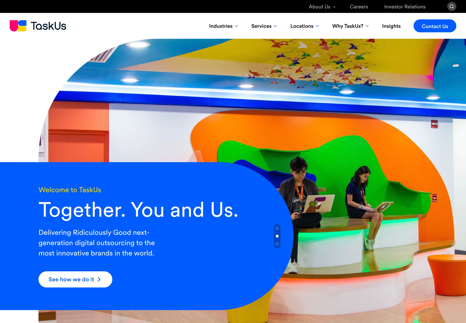 TaskUs's homepage in June 2021: two employees working on laptops in a brightly painted office, under the headline 'Together. You and Us.'